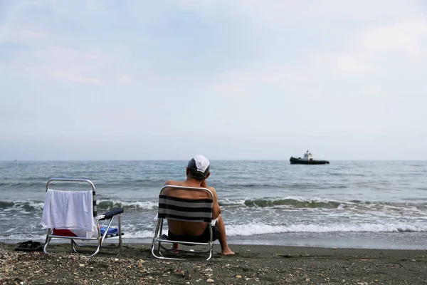 Man sitting on chair is watching an old ship sailing on sea