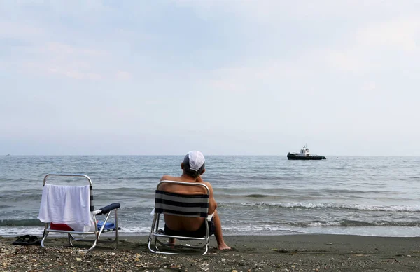 Man sitting on chair is watching an old ship sailing on sea