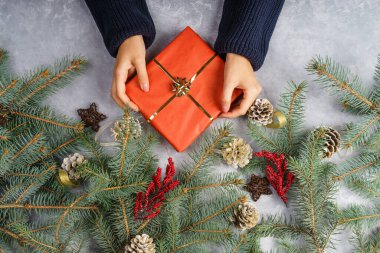 Kadın eller bir hediye tutuyor. Gri bir zeminde altın bir fiyonk olan kırmızı bir kutu. Bayramlar için bayram arkaplanı: Noel, Yeni Yıl. Düz yatıyordu.