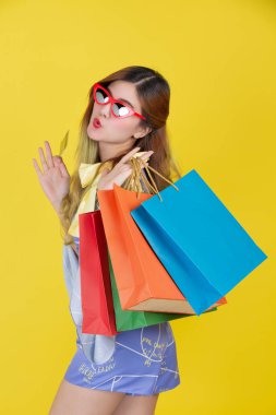 The girl holds a fashion shopping bag and holds a smart card on a yellow background.