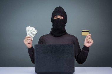 Thieves hold credit cards using a laptop computer for password hacking activities. Cyber crime concepts.