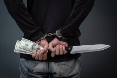 Yüzünü gizleyen siyah şapkalı hırsız, gri bir arka planda tutuklandı..