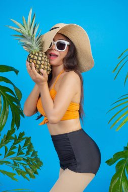 Mavi arka planda ananas tutan mayolu güzel bir kadın..