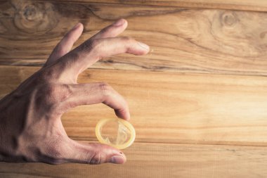 Kondomlar, ahşap arka planda el kol hareketleri yapan adamların elinde..