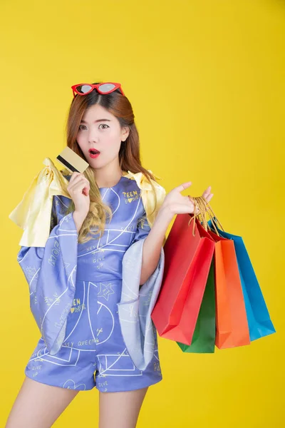 The girl holds a fashion shopping bag and holds a smart card on a yellow background.