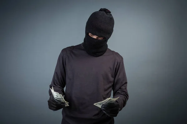 Criminals wear black masks to hold dollar cards on a gray background.