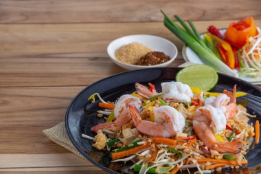 Pad Thai, siyah bir tabakta taze karides, ahşap bir masaya yerleştirilmiş..