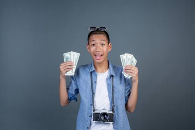 Genç turistler kameralarını boyunlarına asıyor ve gri arka planda dolarları tutuyorlar..