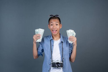 Genç turistler kameralarını boyunlarına asıyor ve gri arka planda dolarları tutuyorlar..