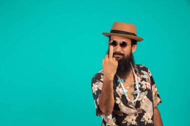 Uzun sakallı, şapkalı, çizgili tişörtlü mutlu bir adamın mavi arka planda bir jest göstermesi..