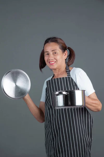 An elderly cook with kitchenware in his hand on a gray background.
