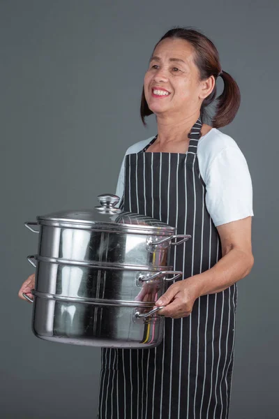 An elderly cook with kitchenware in his hand on a gray background.