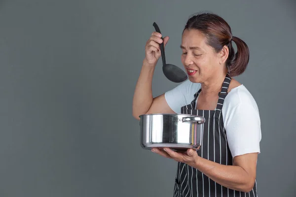 An elderly cook with kitchenware in his hand on a gray background.