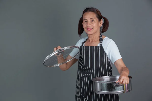 An elderly cook with kitchenware in his hand on a gray background.