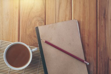 Kahverengi ahşap zemindeki kitabın yanına koyulmuş kahve..