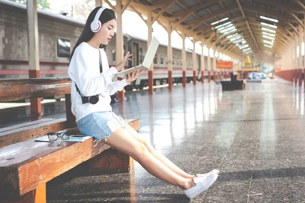 Women are listening to music and playing notebooks while waiting for the train. Tourism concept