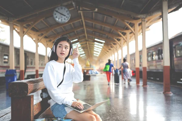 Women are listening to music and playing notebooks while waiting for the train. Tourism concept