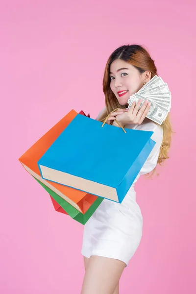 The girl holds a fashion shopping bag and holds a dollar card on a pink background.