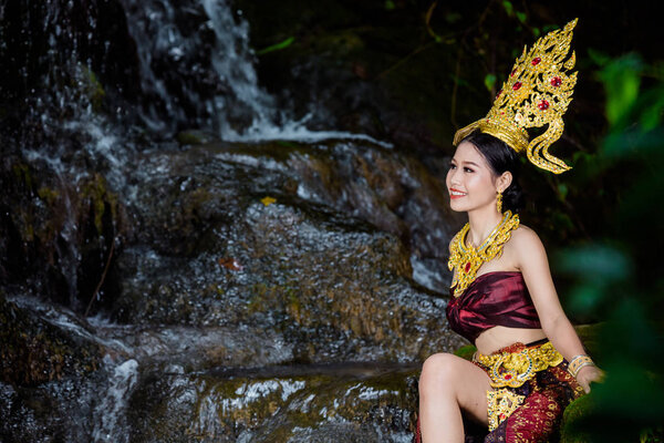 Женщина, одетая в древнее тайское платье у водопада.