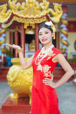 Güzel bir Asyalı kız kırmızı bir takım elbise giyiyor. Hareketlerini gösteriyor ve gülümsüyor. Onu mutlu gösteriyor..