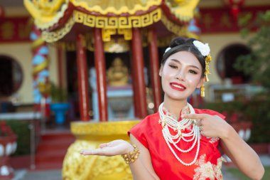 Güzel bir Asyalı kız kırmızı bir takım elbise giyiyor. Hareketlerini gösteriyor ve gülümsüyor. Onu mutlu gösteriyor..