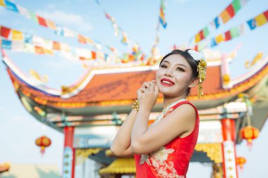 Güzel bir Asyalı kız kırmızı bir takım elbise giyiyor. Hareketlerini gösteriyor ve gülümsüyor. Onu mutlu gösteriyor..