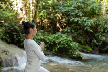 Güzel kızlar parkta yoga oynuyorlar. Ormandaki doğal şelaleler arasında egzersiz konseptleri
