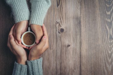 İki insan ellerinde bir fincan kahveyle sevgi ve sıcaklığı ahşap masada tutuyorlar.