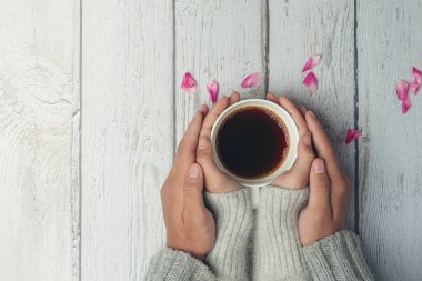 İki insan ellerinde bir fincan kahveyle sevgi ve sıcaklığı ahşap masada tutuyorlar.