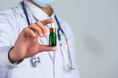 Sağlık doktorunun beyaz arka planda elinde bir şişe kenevir yağı tutarken çekilmiş resmi..