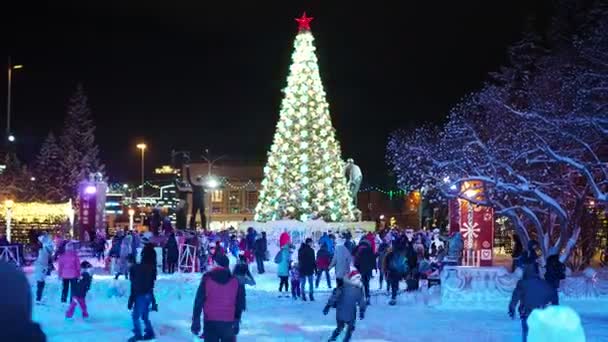 クリスマス 夜の街 クリスマスツリーの輝く照明を背景に 雪に覆われたスケートリンクに乗って街の住民 シベリアのノヴォシビルスク — ストック動画