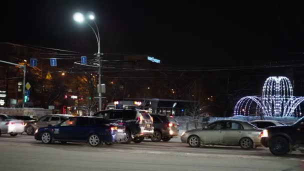 겨울밤 거리에서 차들이 램프로 분수를 지나고 시베리아 노보시비르스크 — 비디오