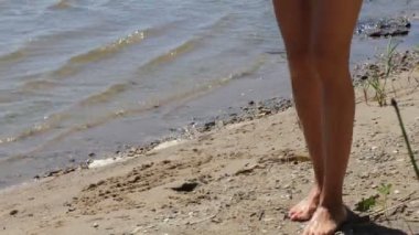 Kadın, plaj. Güneşli bir günde kumlu bir sahilde kadınların ayakları sığ sularda yürür. Kapat..