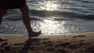 Kumsal. Suyun kenarındaki dalgalar sırasında kumlu bir plajda yürüyen insanların siluetleri. Yakınlaştırıyorum. Yavaş çekim.