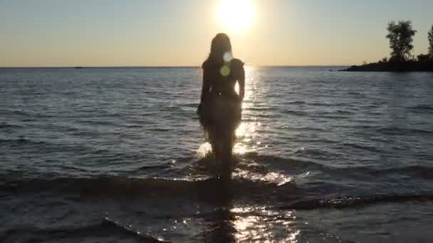 日落时在海滩上的女孩 一个穿着漂亮衣服的女孩在日落时分穿过阳光小径进入水里去了 西伯利亚的奥布河慢动作 — 图库视频影像