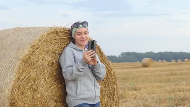 Kız Bir Tarlada Saman Balyasının Yanında Dururken Telefonuna Bakar Yakınlaştırılıyor — Stok video