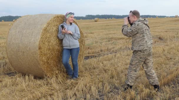 Mężczyzna Kamuflażu Fotografuje Dziewczynę Która Stoi Pobliżu Beli Słomy Polu — Wideo stockowe