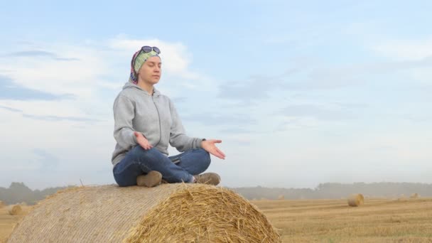 Lotus Pozisyonunda Bir Kadın Bir Tarlada Saman Balyasının Üzerinde Oturuyor — Stok video