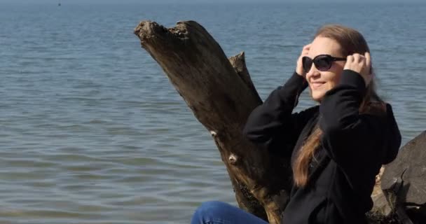 一个年轻的快乐的女人坐在水边的树干上 笑着把头发理直 西伯利亚Ob河 — 图库视频影像