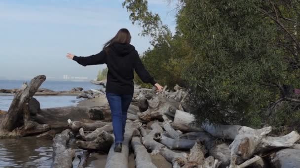 一位年轻妇女沿着树干走着 树干被水流冲到河岸 慢动作 奥布河 西伯利亚 — 图库视频影像
