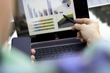 İşadamı, dizüstü bilgisayar ve tablet kullanarak bir grafikle finansal rakamları analiz ediyor.