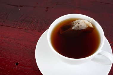 kahverengi ahşap masa yüzeyinde çay poşeti ile çay fincanı