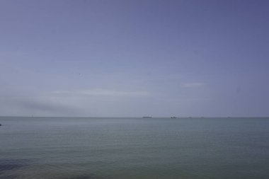 Kumlu sahil ve ufukta gemileri ve tekneleri olan sakin deniz suyu. 