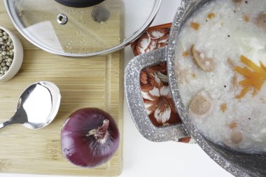 Beyaz arka plan üzerinde soğan, kaşık ve biberli sıcak kapta lapa.