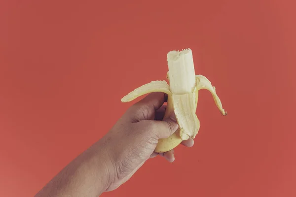 Рука Человека Держит Один Желтый Банан Красном Фоне — стоковое фото