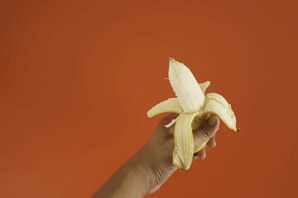 赤い背景の上にバナナを保持する男性の手 — ストック写真