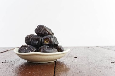 Plakalı kahverengi ahşap masa yüzeyinde beyaz kase tabaktabaktabaktabaktabakmeyveleri tarihler 