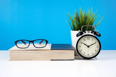 mavi duvara karşı kapalı kitap gözlük, pota bitki ile alarm vintage analog saat 