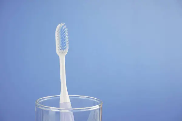 Uma Escova Dentes Com Cerda Copo Vidro Contra Fundo Azul — Fotografia de Stock