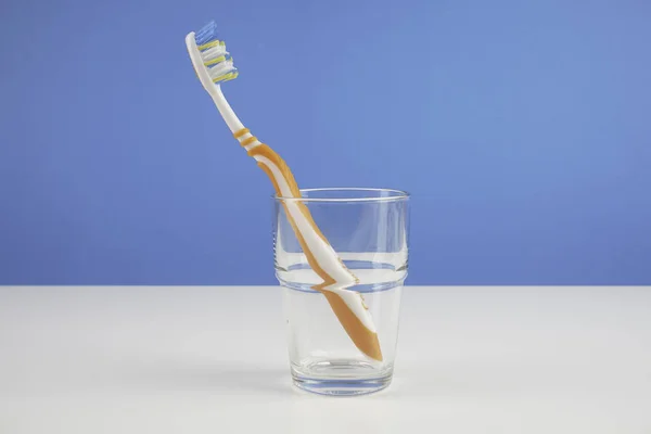 一个牙刷与刷毛在玻璃杯蓝色背景 — 图库照片